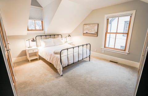 Loft bedroom with slanted ceiling, black metal bed frame, white linens, and warm morning light.