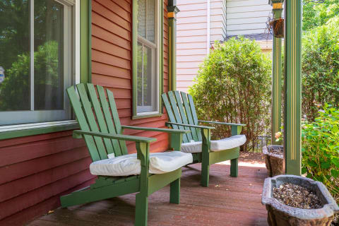 Two green Adirondack chairs with white cushions on a inviting porch surrounded by greenery.