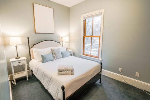A cozy bedroom with a neatly made bed, plush pillows, and a window showing snow outside.