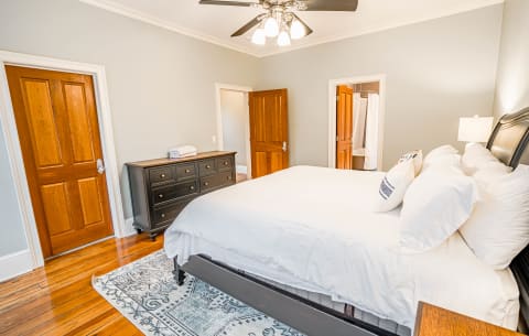 A well-furnished bedroom with a king bed, dark dresser, and pale walls, creating a cozy atmosphere.