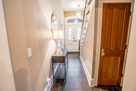 A sophisticated entryway with a console table, lamp, and staircase, illuminated by natural light.