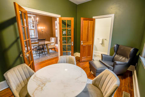 Sitting area featuring green walls, marble table, and leather chairs adjacent to a dining room.