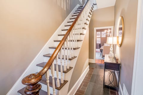 A beautifully designed staircase with hardwood steps and white spindles, accompanied by a stylish console table and lamp in a warm hallway.