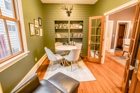 A cozy and intimate dining nook featuring a round marble table, plush chairs, and rich green walls with built-in shelves.
