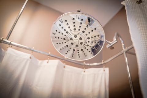 A close-up view of a modern rainfall showerhead above a white shower curtain in a soft-lit bathroom.