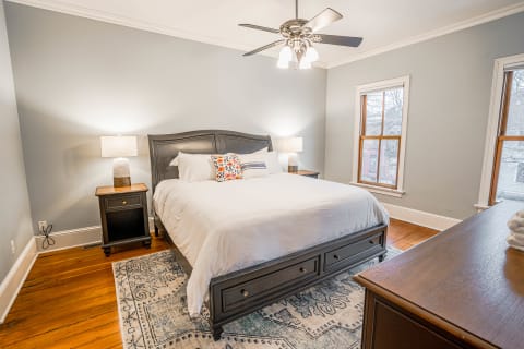 A tranquil bedroom with a large bed, colorful throw pillows, nightstands with lamps, and natural light from windows.