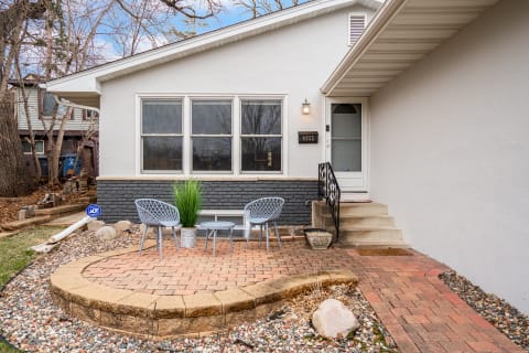 A modern home exterior featuring a brick patio and stylish outdoor seating in a tranquil neighborhood.
