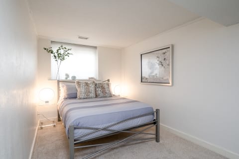 A serene bedroom with a silver bed frame, plush pillows, a warm lamp, and soothing decor.