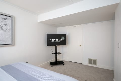 A spacious bedroom with a wall-mounted TV, soft bedding, and abstract art on the walls.