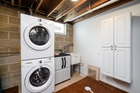 Laundry room with stacked washer and dryer, utility sink, and white cabinets.