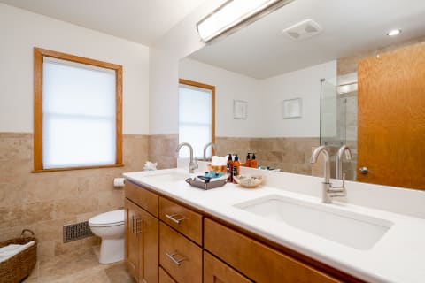 A modern bathroom with dual sinks, wooden cabinetry, and natural light streaming through a window.