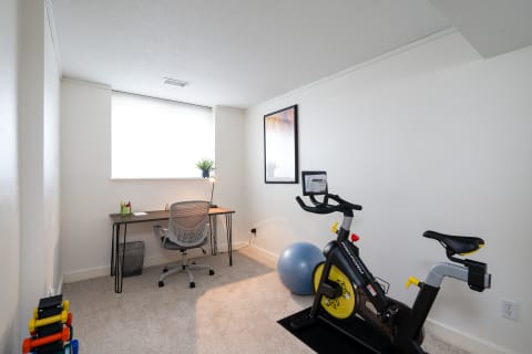 A bright, organized home office with a desk, chair, and exercise bike in a cozy environment.