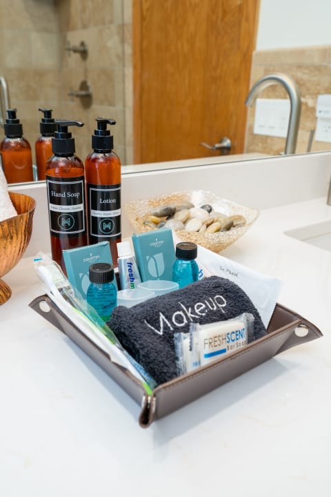 Bathroom countertop with an elegant display of hand soap, lotion, and a tray of assorted toiletries, including a towel and small bottles.
