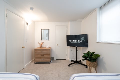 Cozy bedroom with a flat-screen TV and a wooden dresser, showcasing a modern design.