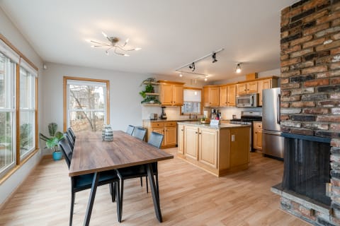 Open kitchen and dining area with wooden cabinets, dining table, and exposed brick fireplace.