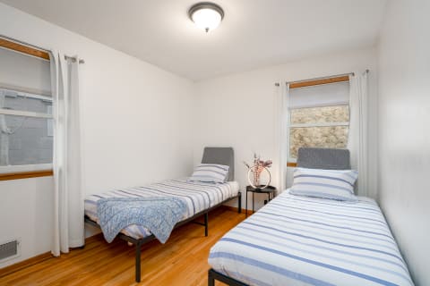 A cozy twin bedroom featuring striped beds, a bedside table with a glowing lamp, and natural light.