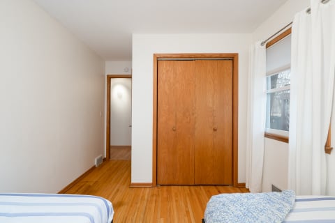A spacious bedroom with hardwood floors and a wooden sliding wardrobe, decorated in soft colors and natural light.