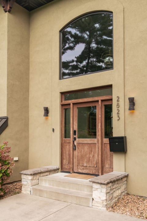 A close-up view of a modern home entrance featuring wooden double doors, large arched window, and stylish light fixtures.