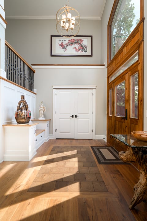 A modern entryway featuring wooden floors, a chandelier, and decorative sculptures.