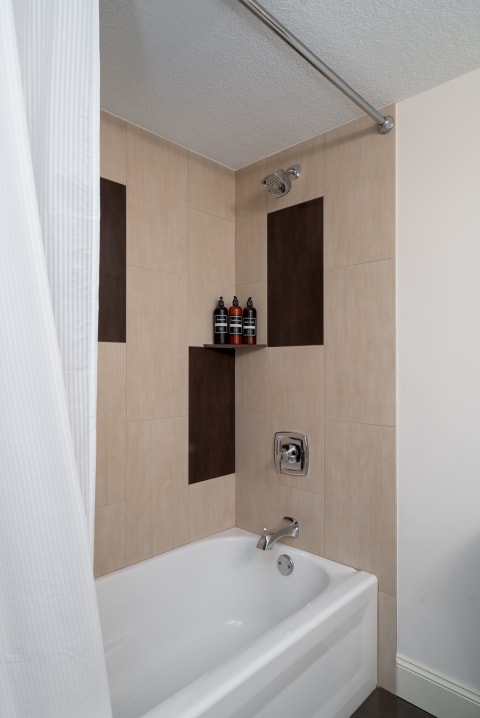 A contemporary bathroom with beige and brown tiles, a showerhead, and neatly arranged shampoo bottles.