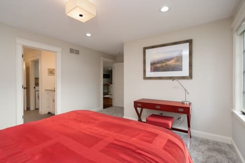A contemporary bedroom featuring a red bedspread, a stylish red desk, and a coastal landscape photograph on the wall.