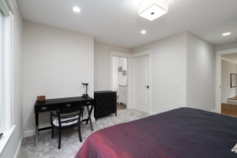 A modern bedroom with a gray color scheme, black desk, red bedspread, and decorative cabinet.