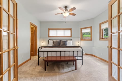 A cozy bedroom featuring a black metal bed, wooden bench, and light blue walls with natural light from windows.