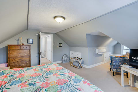 A warm attic bedroom with a sloped ceiling, a floral bedspread, and comfortable seating.