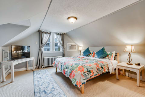 A vibrant attic bedroom with floral bedding, TV, and window.