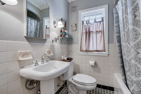 A modern bathroom with a pedestal sink, mirror, and decorative curtain.