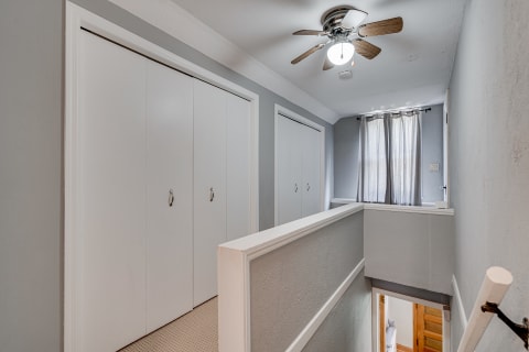 Light-filled upstairs hallway featuring white closet doors and a ceiling fan.