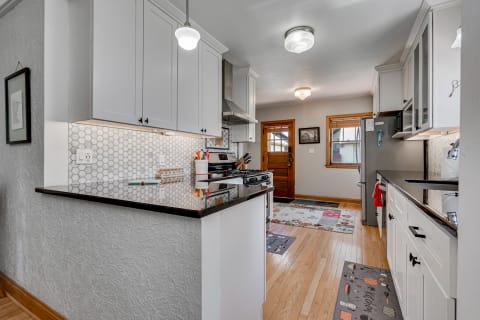 Modern kitchen with white cabinets and black countertop overlooking a wooden door and colorful rugs.