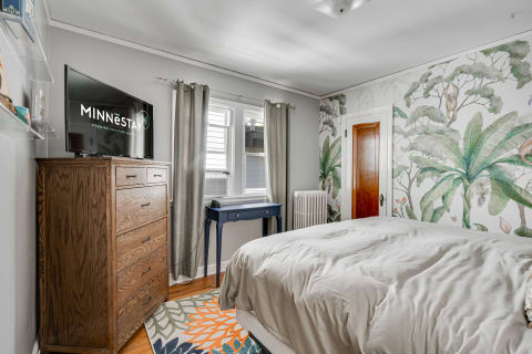 Cozy bedroom featuring a tropical wallpaper mural, a wooden dresser, and a TV.
