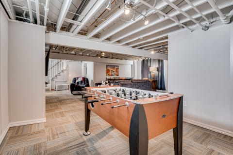 A basement lounge with a foosball table, sofa, and staircase.