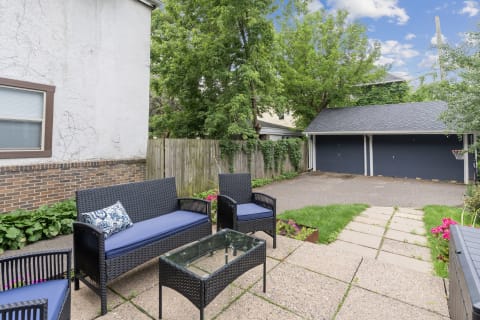 Outdoor patio featuring wicker chairs, a coffee table, and garages in the background.