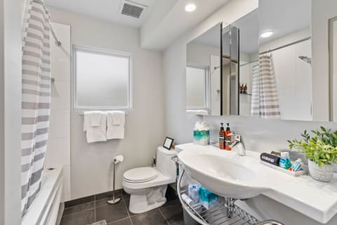 Modern bathroom with a sink, toilet, and shower area, decorated with toiletries and towels.