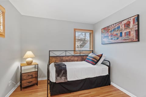 A minimalist bedroom with a single bed, wood nightstand, lamp, and colorful artwork.