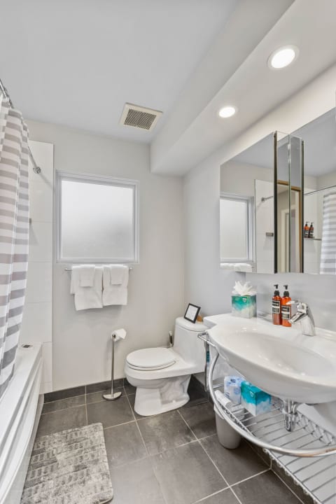 A bright and clean bathroom with a bathtub, sink, and toilet, decorated with towels and toiletries.