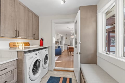 A bright laundry room featuring modern appliances, a quote sign, and a cozy bench.
