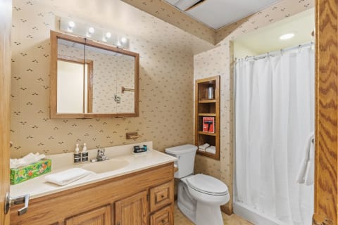 Cozy bathroom with wooden vanity, shower, and vintage wallpaper.