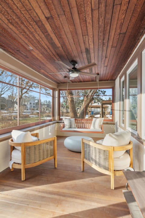 A beautifully designed screened porch with wooden ceilings, comfortable seating, and a swing overlooking a peaceful backyard.