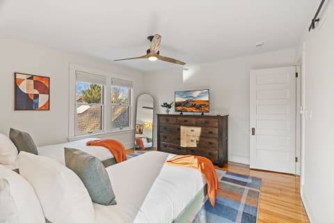 A spacious bedroom with twin beds, a modern artwork on the wall, and a ceiling fan for comfort.