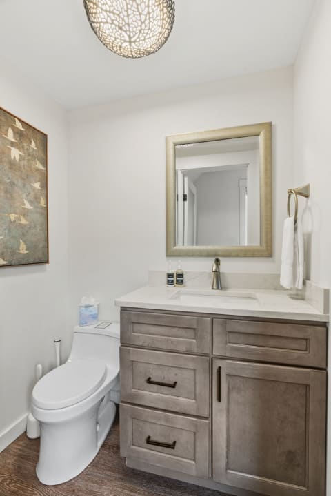 A modern powder room with a marble countertop, framed mirror, and decorative light fixture.