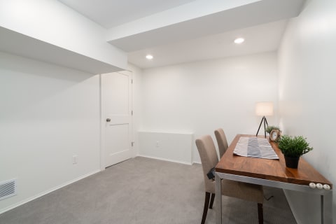 A modern, minimalist room featuring a wooden desk, beige chairs, and a small lamp.