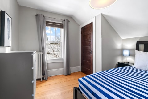 A cozy bedroom with a striped bed, gray dresser, and a view of a tree outside the window.