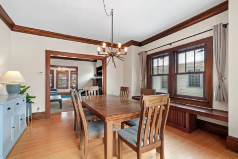 Bright dining room featuring wooden furniture, modern chandelier, and large windows.