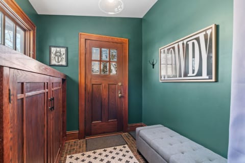 Entryway featuring green walls, a wooden door, decorative art, and a gray bench.