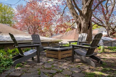 A cozy outdoor seating area with Adirondack chairs around a fire pit, surrounded by autumn foliage.