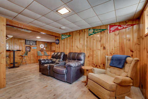 Cozy basement lounge with wooden walls, recliner chairs, and sports memorabilia.
