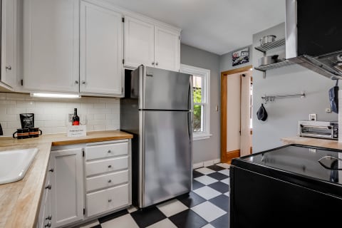 A bright and modern kitchen with white cabinets, a stainless steel fridge, and black and white checkered floor tiles.